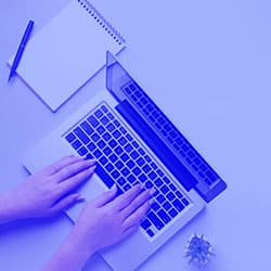 Hands typing on laptop with notebook and pen nearby.